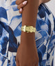 Gold GUESS Ladies Gold Tone Analog Watch on a wrist with a blue and white patterned background
