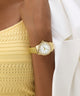 Gold wristwatch on a person wearing a yellow top and white jacket