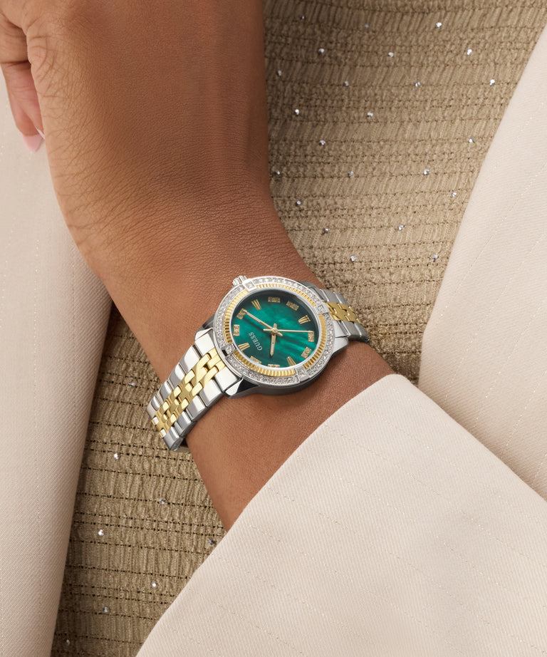 Close-up of a wrist wearing a silver and gold GUESS Ladies Colette 2-Tone Analog Watch with a green face.