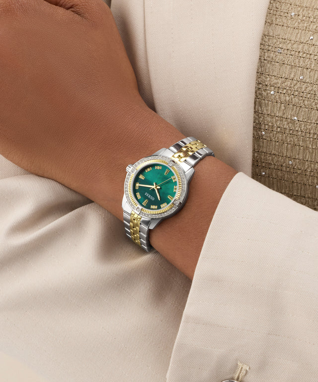 GUESS Ladies Colette 2-Tone Analog Watch with green face and gold accents on a wrist, wearing a beige suit.