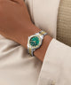 GUESS Ladies Colette 2-Tone Analog Watch with green face and gold accents on a wrist, wearing a beige suit.