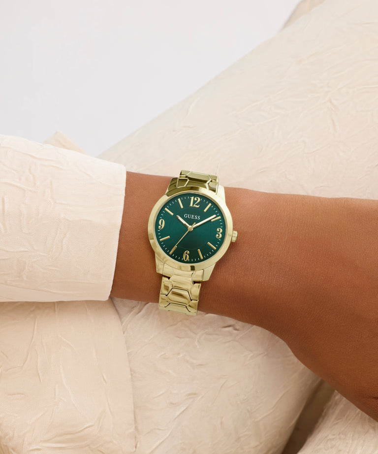 Gold watch with a green face on a wrist against a neutral background