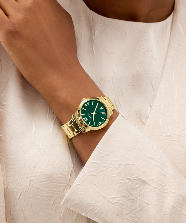 Gold watch with a green face on a wrist against a white fabric background