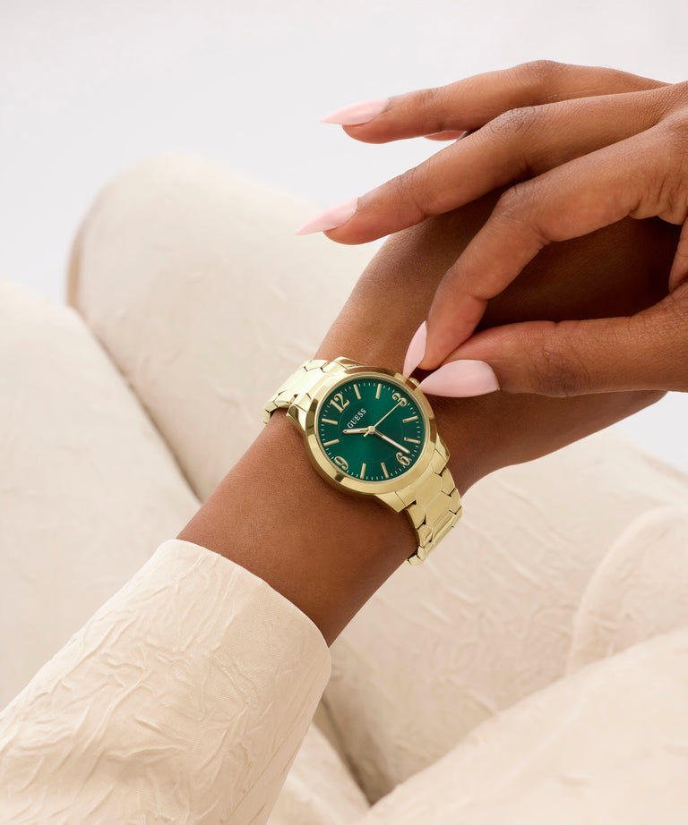 Gold watch with a green face on a wrist, against a neutral background