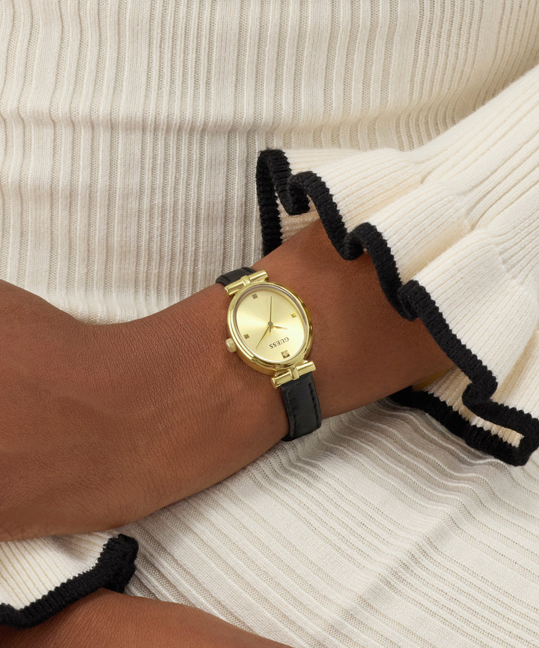 Gold watch on a wrist with a black strap against a neutral background