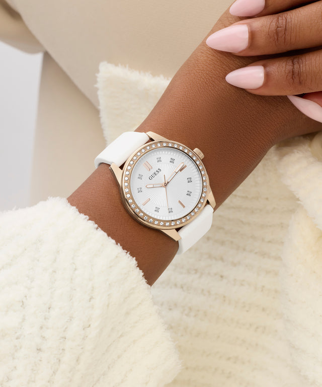 Rose gold watch with white strap on a wrist against a beige background