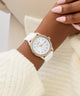 Rose gold watch with white strap on a wrist against a beige background