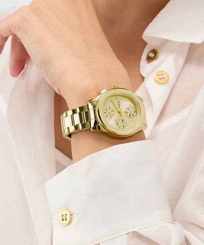 Gold GUESS Ladies Birdie Gold Tone Analog Watch on a wrist with a white shirt background