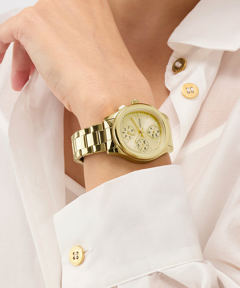 Gold GUESS Ladies Birdie Gold Tone Analog Watch on a wrist with a white shirt background