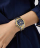 Gold and silver GUESS Ladies Birdie 2-Tone Analog Watch on a wrist with a blue dress