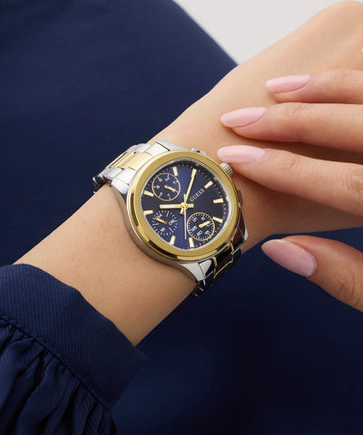 Gold and silver GUESS Ladies Birdie 2-Tone Analog Watch on a wrist with a blue background