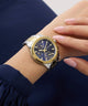 Gold and silver GUESS Ladies Birdie 2-Tone Analog Watch on a wrist with a blue background