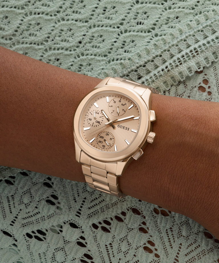 Gold GUESS Ladies Birdie Rose Gold Tone Analog Watch on a wrist with a lace background