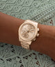 Gold GUESS Ladies Birdie Rose Gold Tone Analog Watch on a wrist with a lace background
