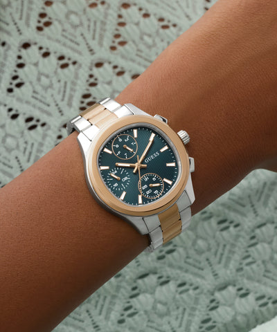 Wrist wearing a two-tone GUESS Ladies Birdie 2-Tone Analog Watch with a detailed face on a textured background