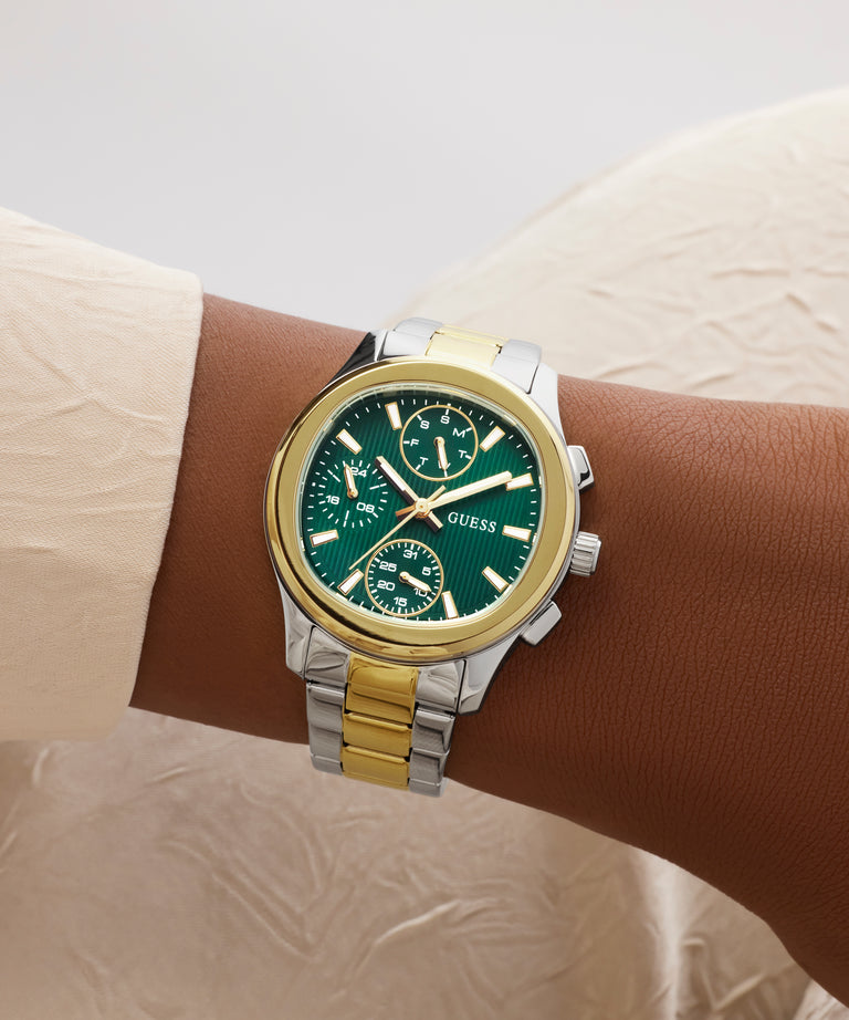 Wrist wearing a Guess watch with a green face and gold accents on a neutral background