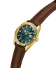 A GUESS wristwatch with a gold-tone fluted bezel, dark blue-green dial, and a brown leather strap, shown on a plain white background. lifestyle
