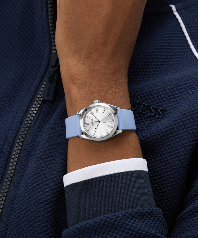 Wrist wearing a GUESS Ladies Blue Silver Tone Analog Watch with a blue strap against a dark jacket background