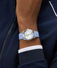 Wrist wearing a GUESS Ladies Blue Silver Tone Analog Watch with a blue strap against a dark jacket background