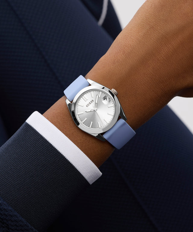 Wrist wearing a watch with a blue strap and silver case, against a dark suit background.