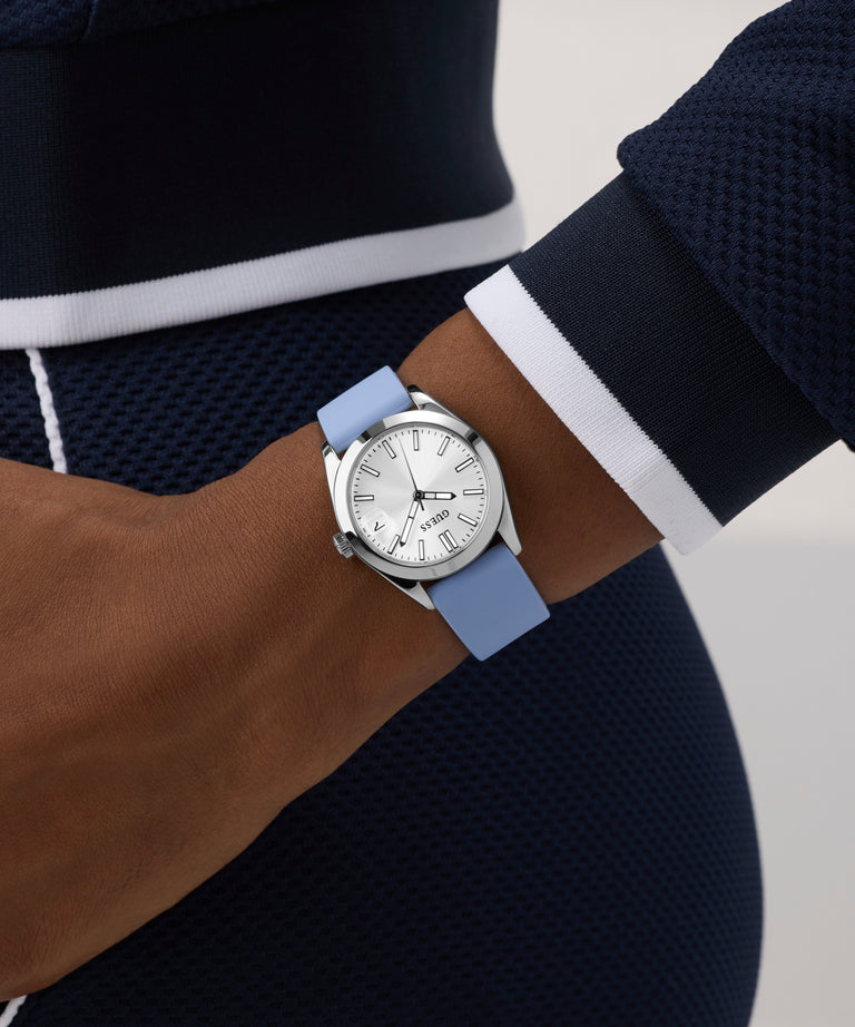 Person wearing a GUESS Ladies Blue Silver Tone Analog Watch with a blue strap on a neutral background