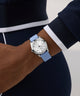 Person wearing a GUESS Ladies Blue Silver Tone Analog Watch with a blue strap on a neutral background