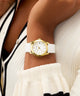 Gold GUESS Ladies White Gold Tone Analog Watch with a white strap on a wrist, wearing a black and white outfit.
