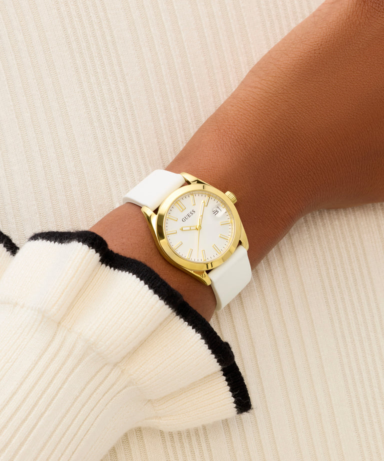 Gold watch with a white strap on a wrist against a neutral background