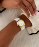 Gold GUESS Ladies White Gold Tone Analog Watch with a white strap on a wrist, with a neutral background