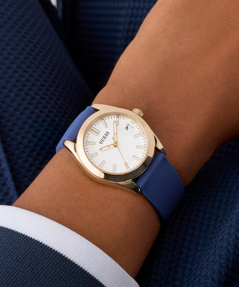 Gold GUESS Ladies Blue Rose Gold Tone Analog Watch with blue strap on a wrist against a dark background