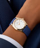 Gold GUESS Ladies Blue Rose Gold Tone Analog Watch with blue strap on a wrist against a dark background