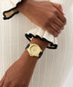 Gold GUESS Ladies White Gold Tone Analog Watch on a wrist with a black strap against a neutral background