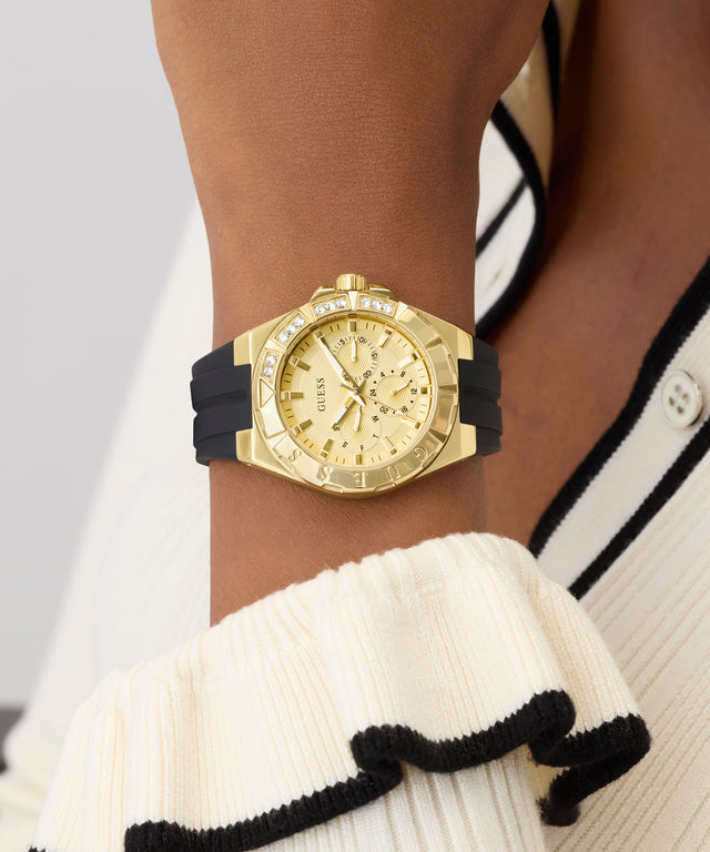 Gold GUESS Ladies White Gold Tone Analog Watch with black strap on a wrist, wearing a white and black outfit.