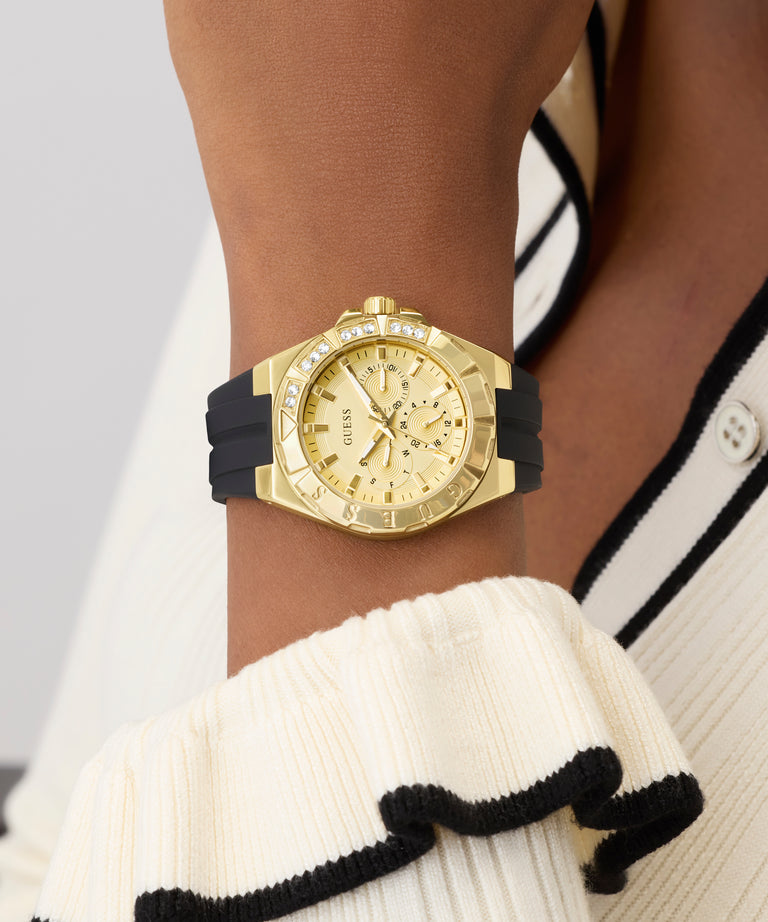 Gold GUESS Ladies White Gold Tone Analog Watch with black strap on a wrist, wearing a white and black outfit.