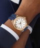 Gold watch with a blue strap on a wrist, wearing a dark blue and white outfit.