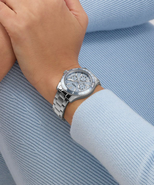 Silver GUESS Ladies Silver Tone Analog Watch on a wrist with a light blue background