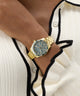 Gold GUESS Ladies Gold Tone Analog Watch on a person's wrist with a white cardigan