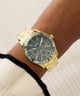 Gold GUESS Ladies Gold Tone Analog Watch with blue face on a wrist against a neutral background