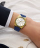 Gold GUESS Ladies Blue Gold Tone Analog Watch with a blue strap on a wrist against a white background