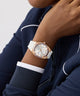 Person wearing a rose gold GUESS Ladies White Rose Gold Tone Analog Watch with a white strap on a plain background
