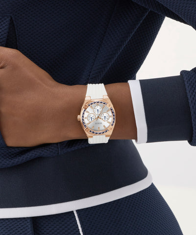 Person wearing a rose gold GUESS Ladies White Rose Gold Tone Analog Watch with a white strap on a blurred background