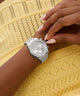 GUESS Ladies Victoria Silver Tone Analog Watch on a wrist with a yellow textured background