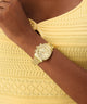 GUESS Ladies Victoria Gold Tone Multi-Function Watch on a wrist with a yellow top