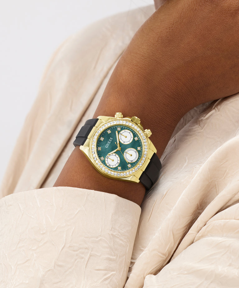 Gold watch with green face on a wrist against a neutral background