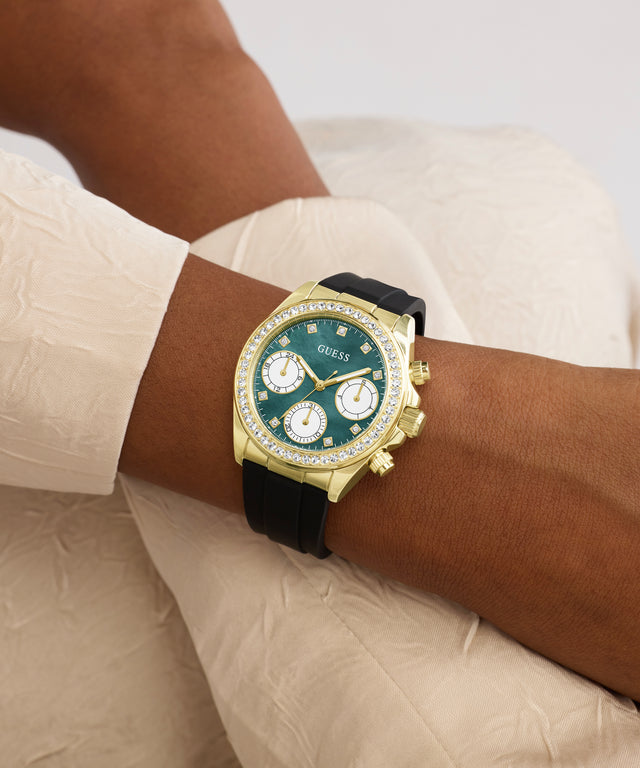 Gold watch with a green face on a wrist, wearing a beige shirt.