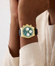 Luxury watch with green face and gold casing on a wrist, against a neutral background