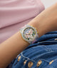GUESS Ladies Blue Analog Watch with gemstones on a wrist, wearing denim jeans with gold buttons.
