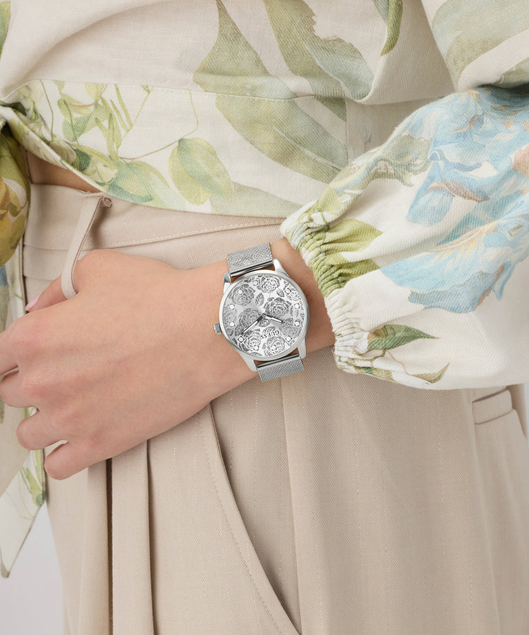 Silver watch on a wrist with a floral-patterned shirt and beige pants