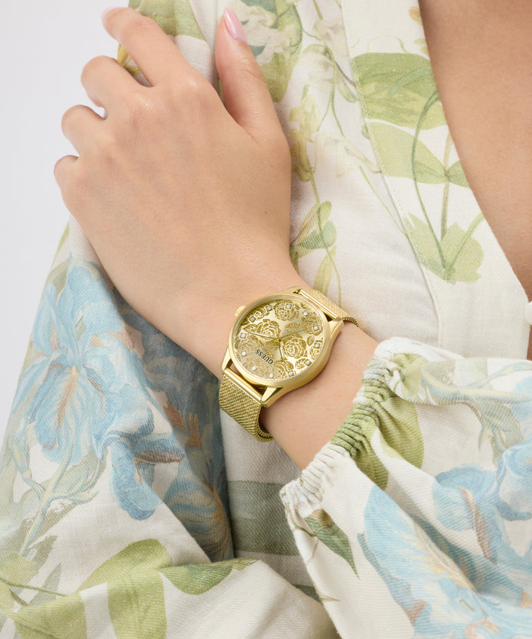 Gold GUESS Ladies Gold Tone Analog Watch on a wrist with floral-patterned fabric background