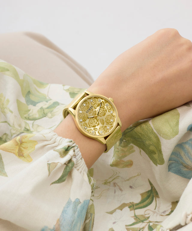 Gold GUESS Ladies Gold Tone Analog Watch on a wrist with floral-patterned fabric background